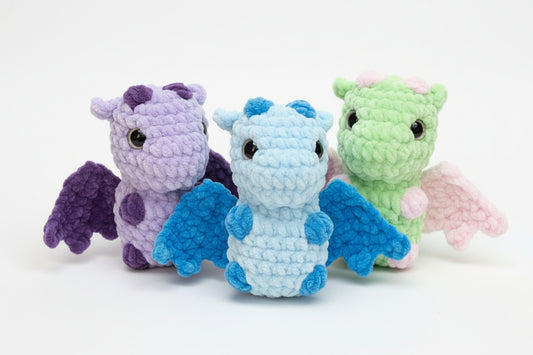 Three small dragon-shaped toys in purple, green, and blue on a textured surface.